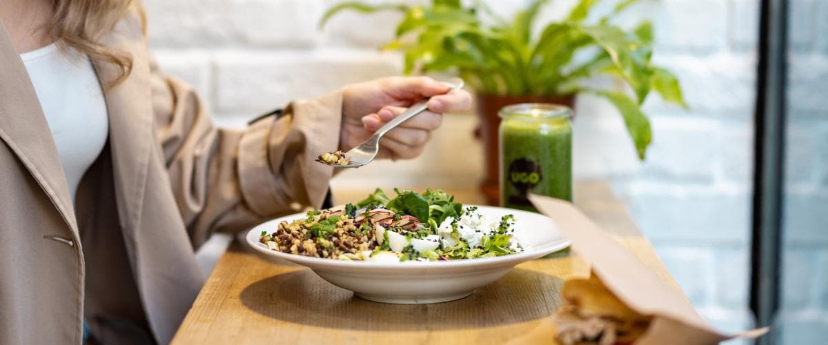 Žena u stolu jí misku s čočkovým salátem a čerstvou zeleninou v UGO bistru.